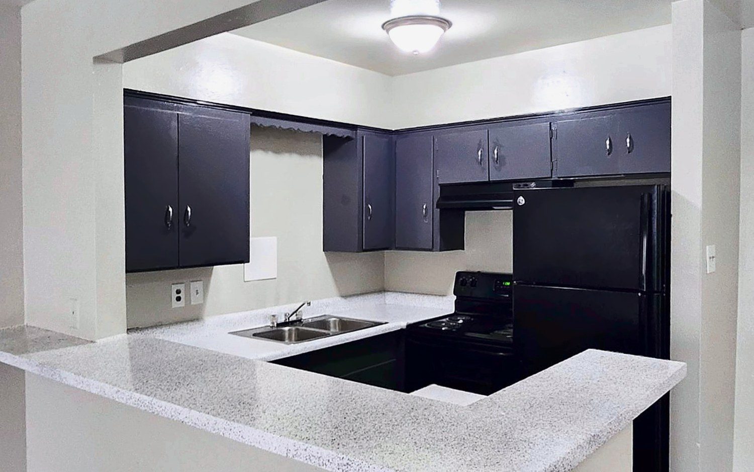 Cocina con gabinetes oscuros, electrodomésticos negros y barra desayunadora