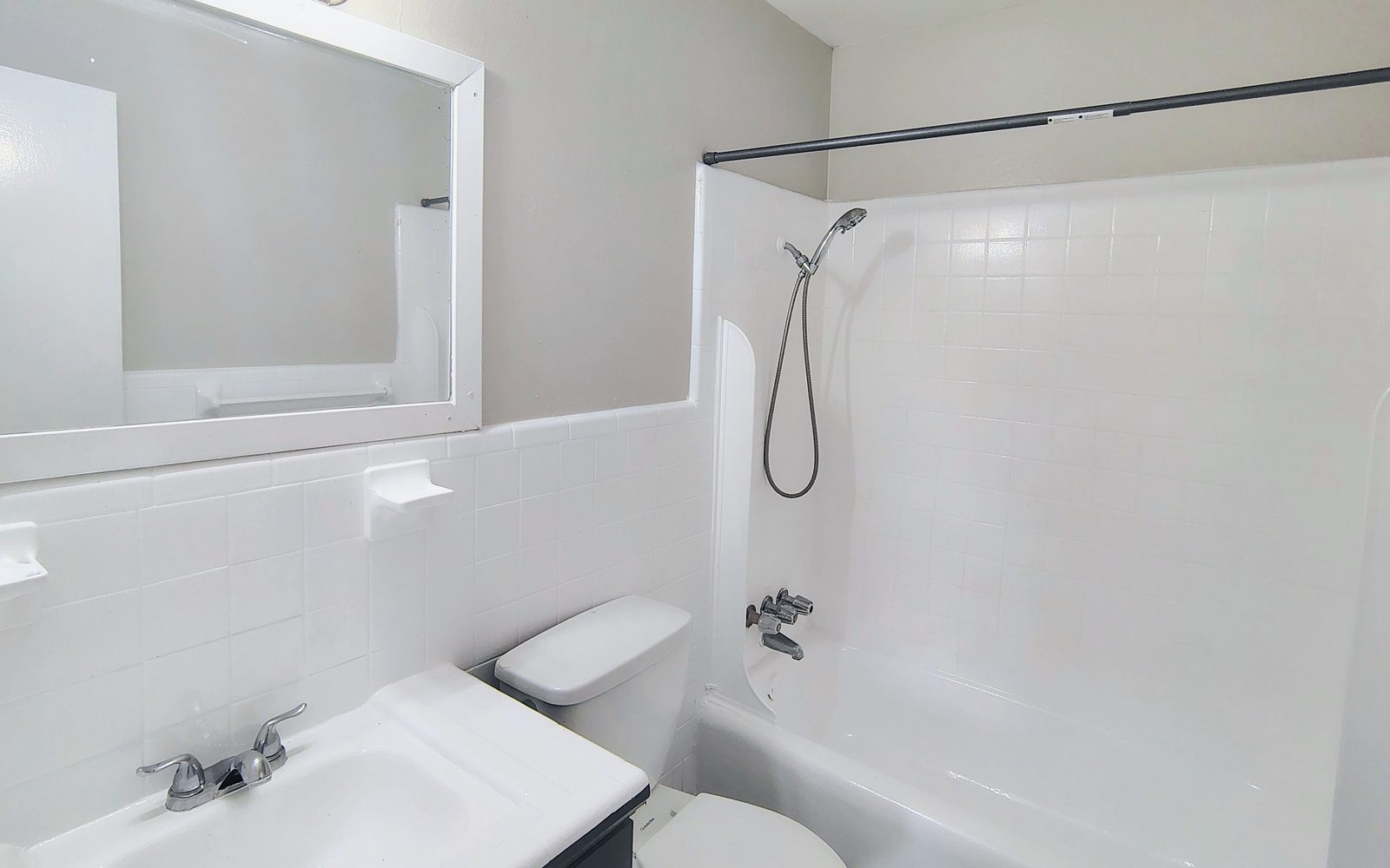 Baño con tina y regadera, lavabo con mueble y un espejo grande