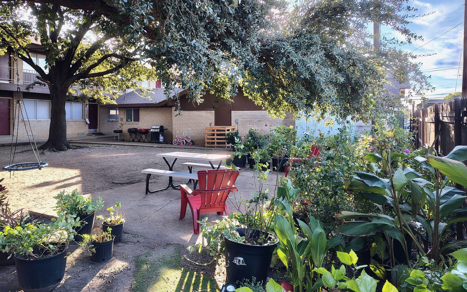 Patio con sombra, una mesa de picnic, una silla roja de jardín y plantas en macetas